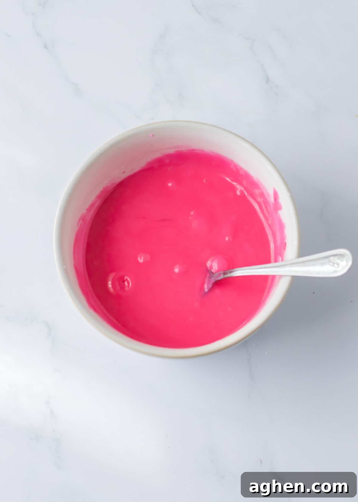 Pink icing in small bowl with spoon.