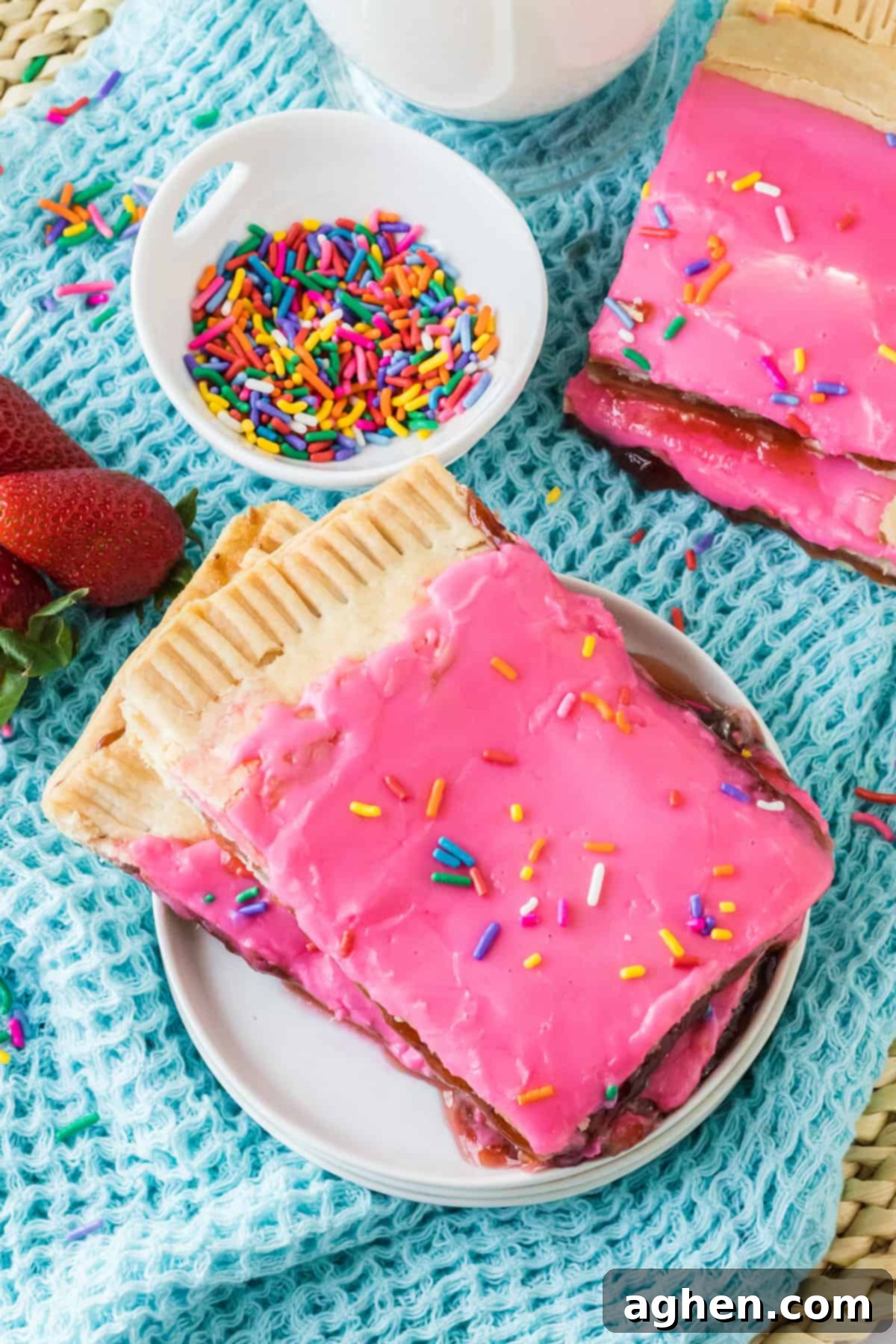 Two large pieces of a giant homemade pop tart on a plate with additional pieces and  sprinkles in the background.