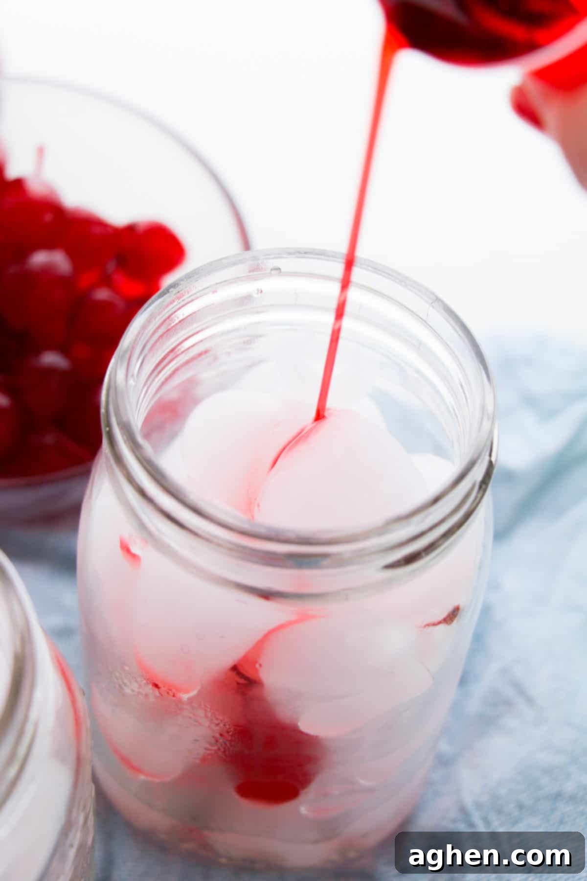 Grenadine being poured into ice-filled mason jar.