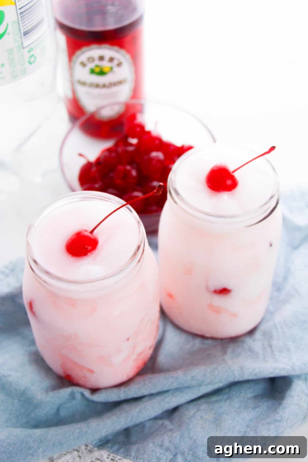 Two Shirley Temple Dirty sodas in mason jars with a bottle of grenadine in the background.