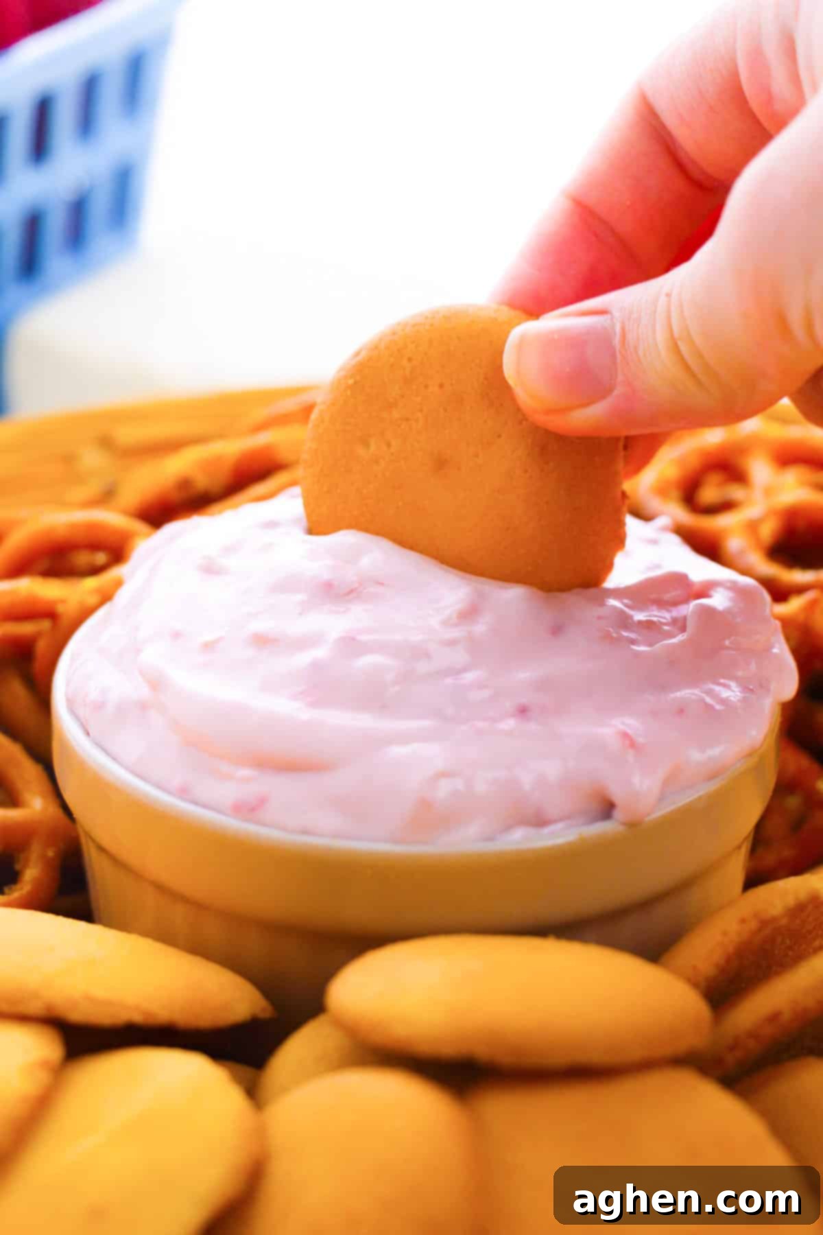 A vibrant bowl of raspberry cream cheese dip, with a vanilla cookie perfectly poised for dipping, showcasing its creamy texture and rich color.