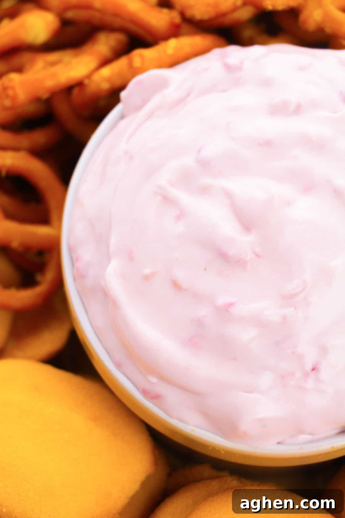 A close-up shot of raspberry cream cheese dip in a decorative bowl, artfully arranged with vanilla wafers and crunchy pretzel twists for dipping.