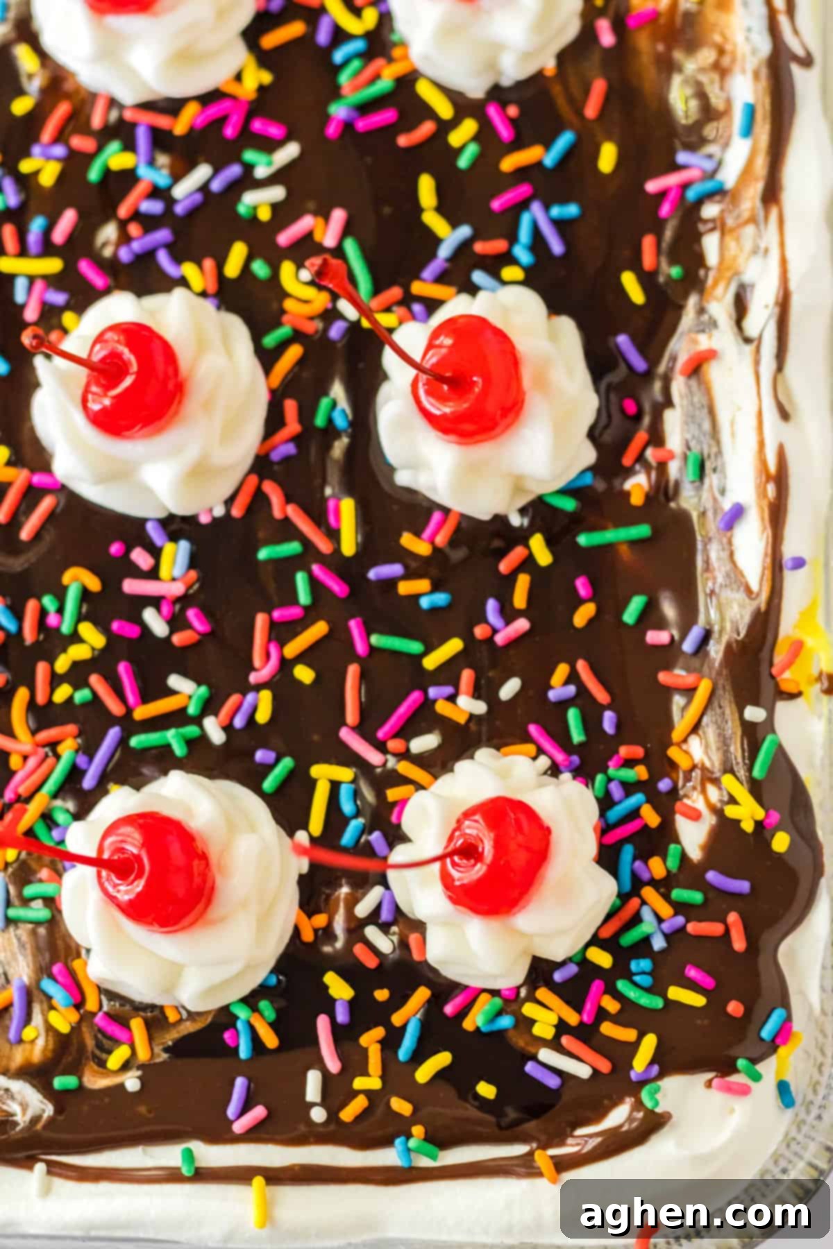 Ultimate No-Bake Banana Split 3 Banana split lush dessert with chocolate sauce, sprinkles, whipped cream, and cherries on top.