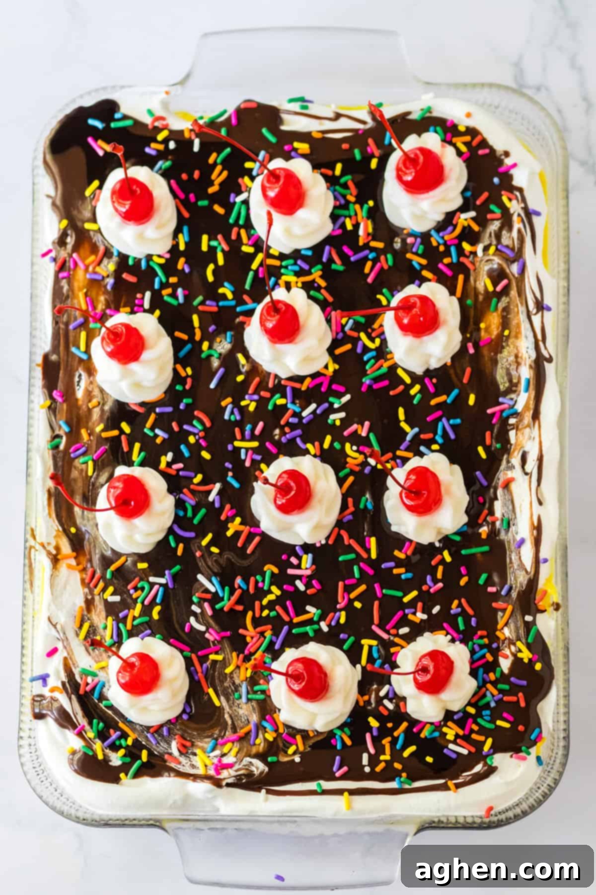Ultimate No-Bake Banana Split 9 Dessert topped with chocolate syrup, rainbow sprinkles, and 12 dollops of whipped cream each topped with maraschino cherries.