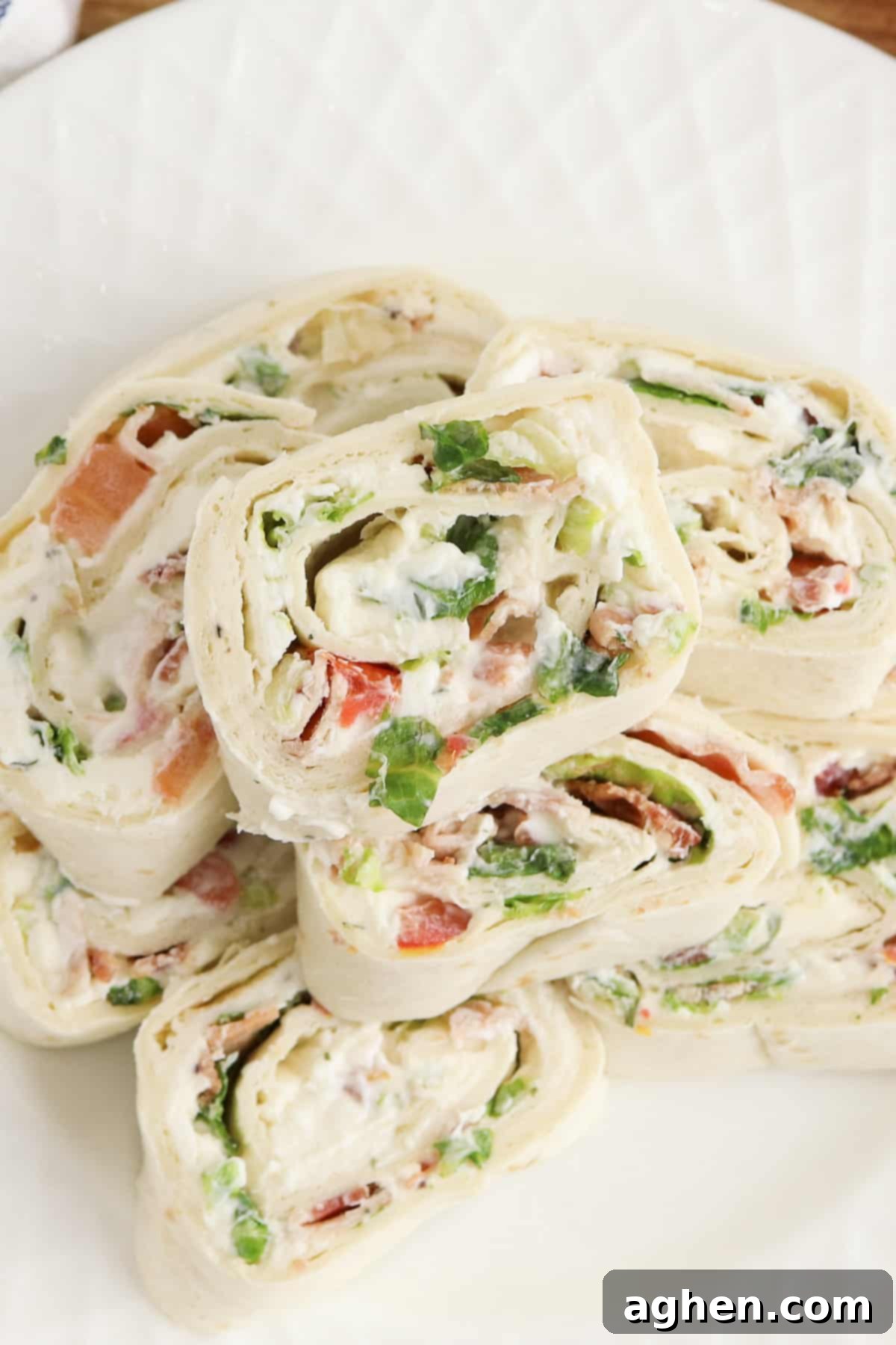 Creamy Ranch BLT Swirls 2 Overhead photo of ranch blt pinwheels stacked on top of one another and served on a white plate, highlighting their vibrant colors and appealing presentation.