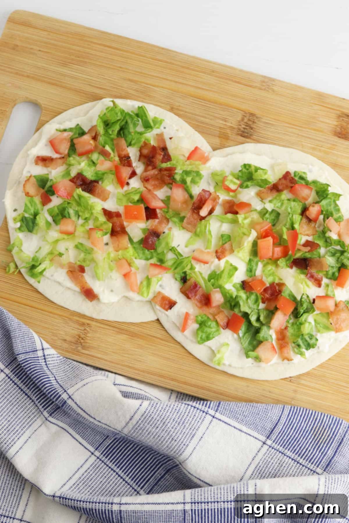 Creamy Ranch BLT Swirls 4 Two flour tortillas laid slightly overlapping on a cutting board, topped with creamy dressing, shredded lettuce, diced tomatoes, and chopped bacon.