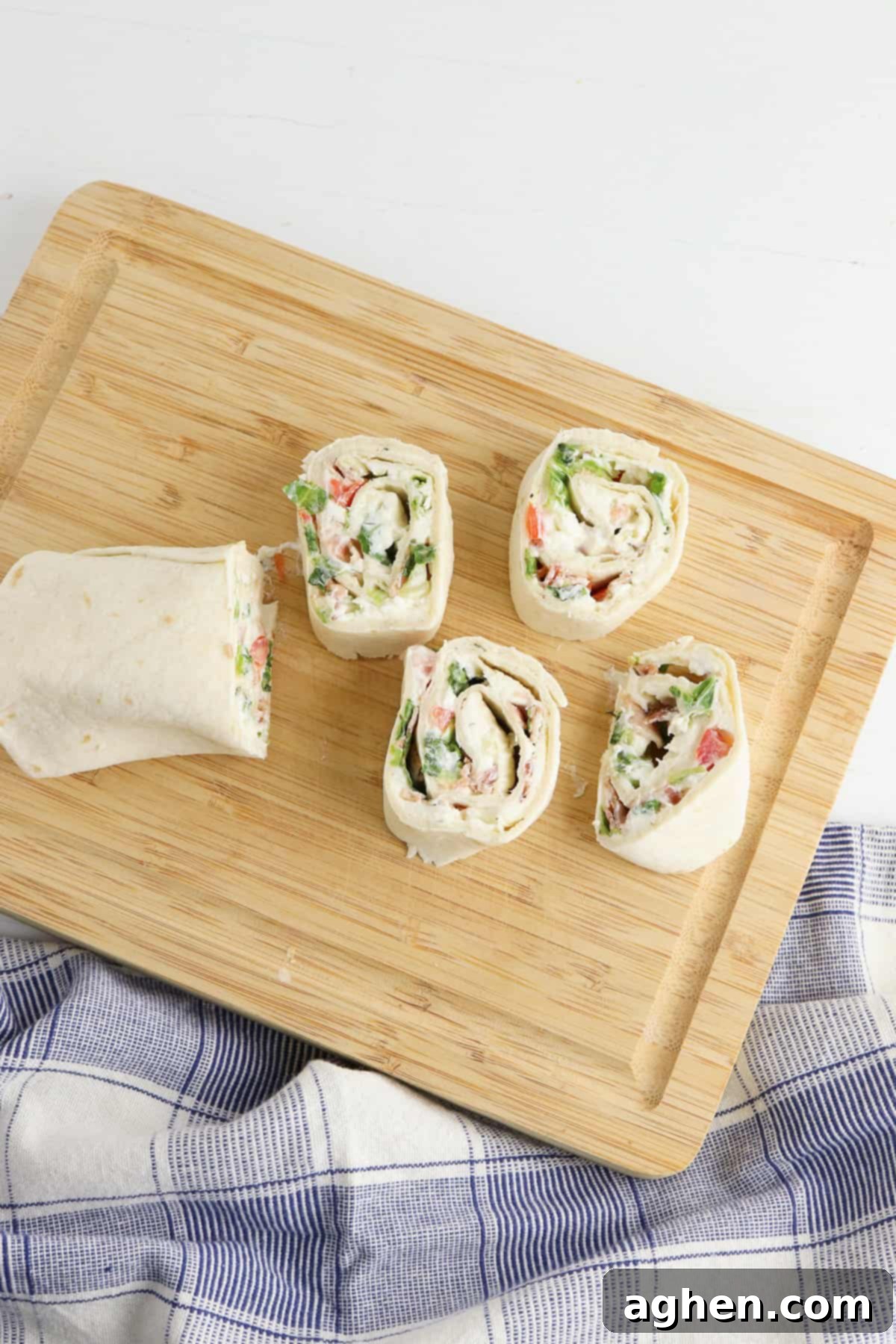 Creamy Ranch BLT Swirls 6 Rolled up tortilla being cut into 1-inch slices on a wooden cutting board, revealing the colorful pinwheel design.