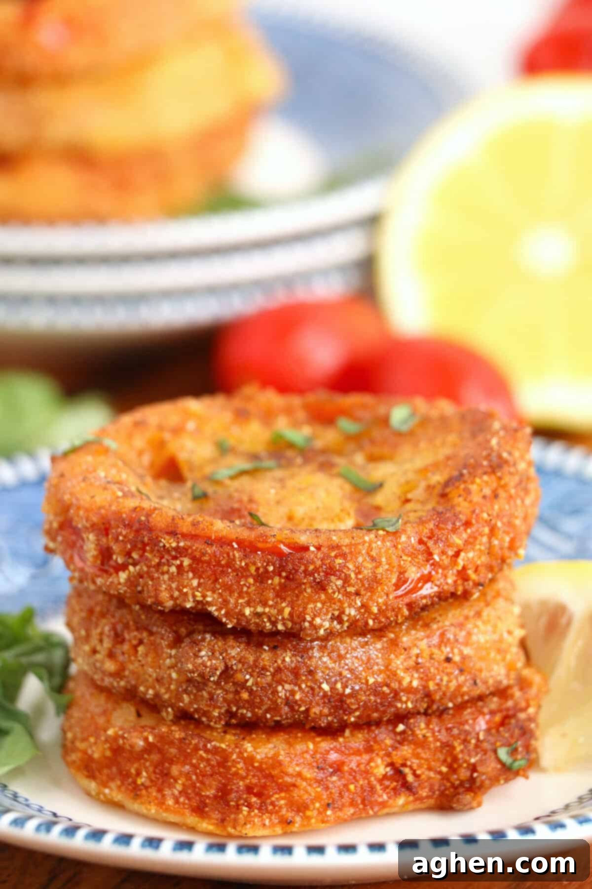 Golden crispy fried red tomatoes arranged on a plate with fresh lettuce, a slice of ripe tomato, and a lemon wedge in the background, hinting at a fresh summer meal.