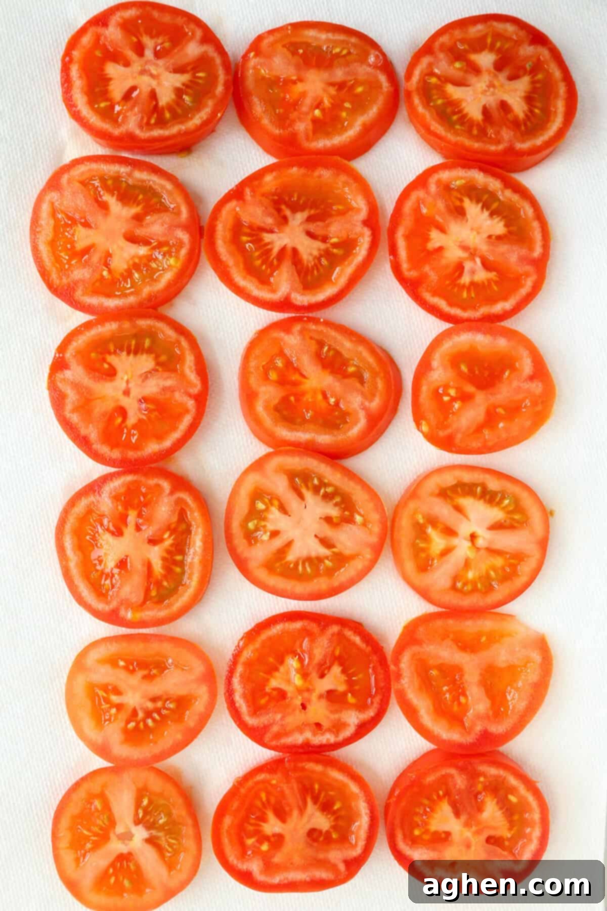 Slices of ripe red tomatoes laid out in a single layer on paper towels on a wire rack to drain excess moisture, lightly seasoned with garlic powder.