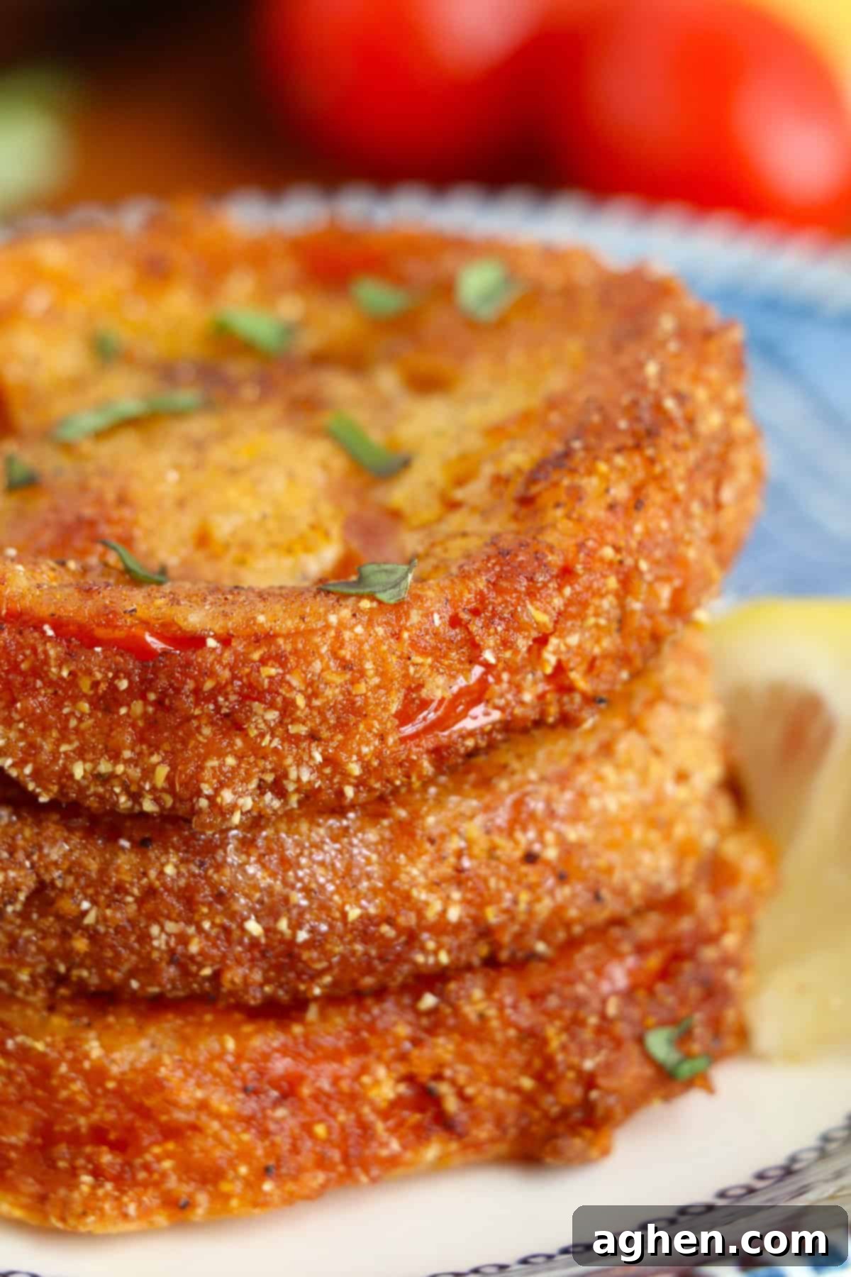 Crispy fried red tomatoes garnished with fresh basil leaves, neatly stacked on a white plate ready for serving, highlighting their golden crust.