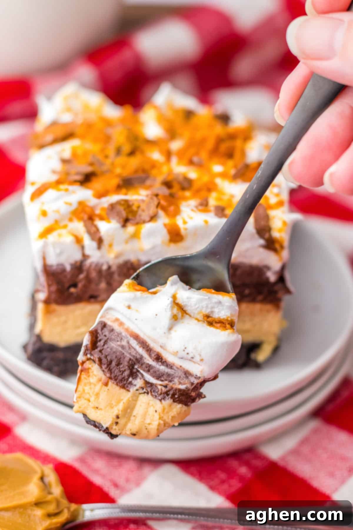 Butterfinger Crunch Layer Dream 5 A spoonful of the layered Butterfinger dessert, showing the distinct layers of Oreo crust, peanut butter cream cheese, chocolate pudding, and whipped topping with crushed Butterfingers.