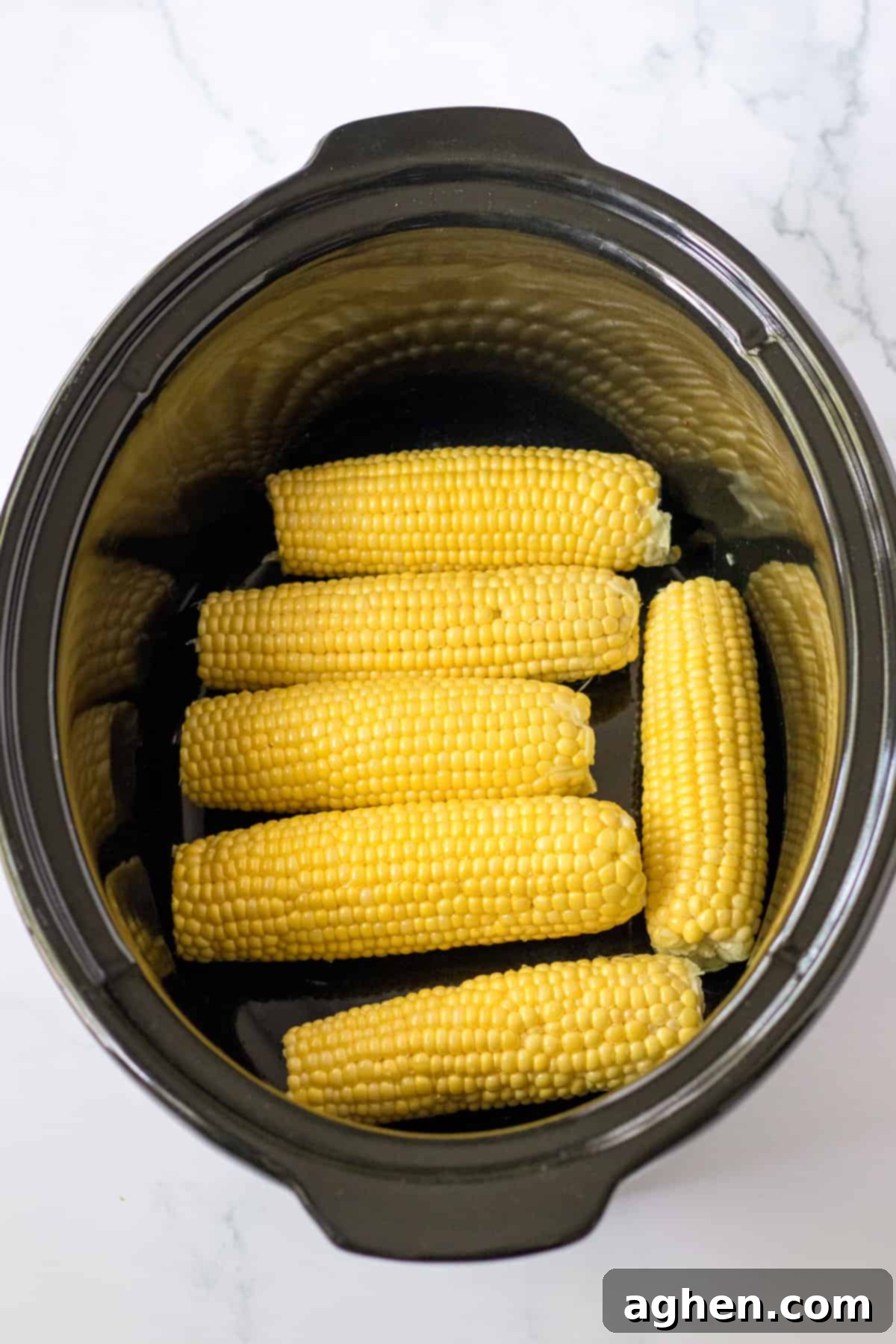 Effortless Slow Cooker Corn 5 Uncooked corn on the cob in an even layer in the bottom of a slow cooker.