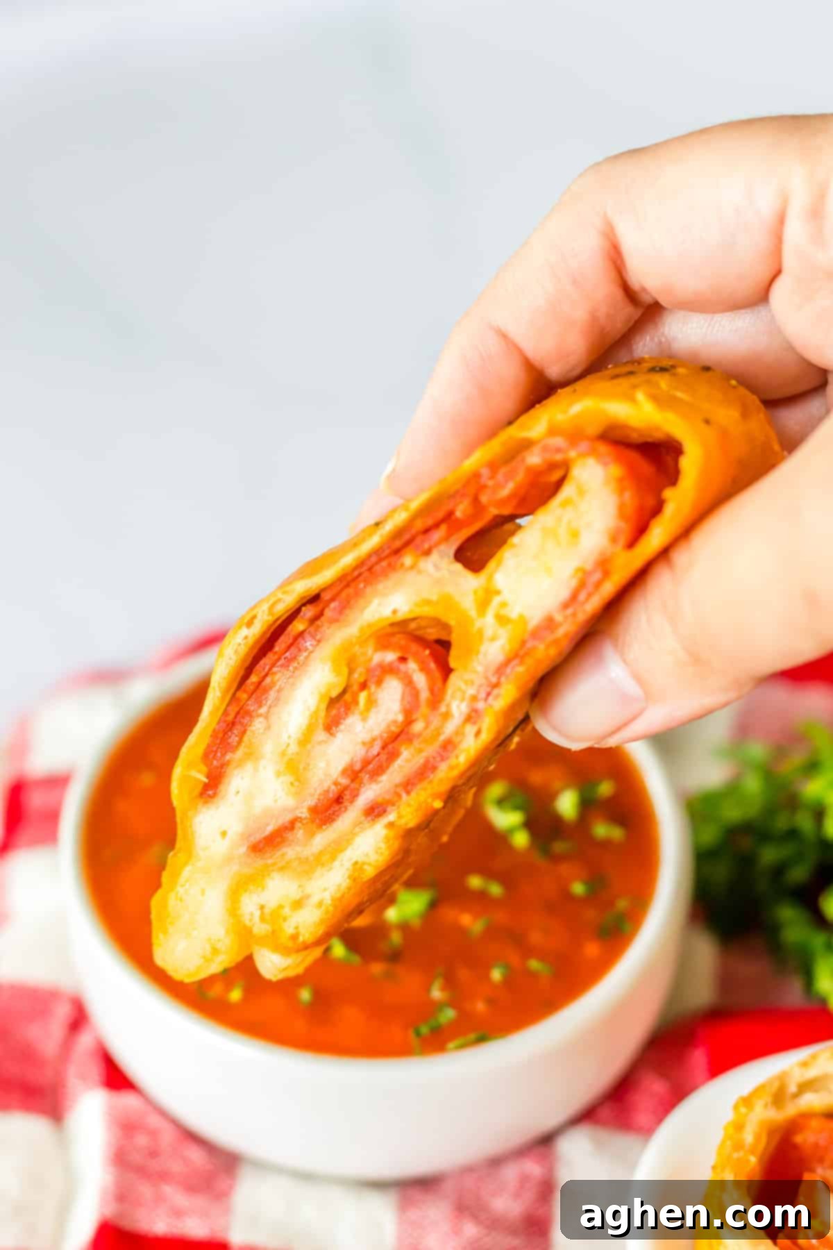 Slice of pepperoni bread being dunked in small bowl of marinara sauce.