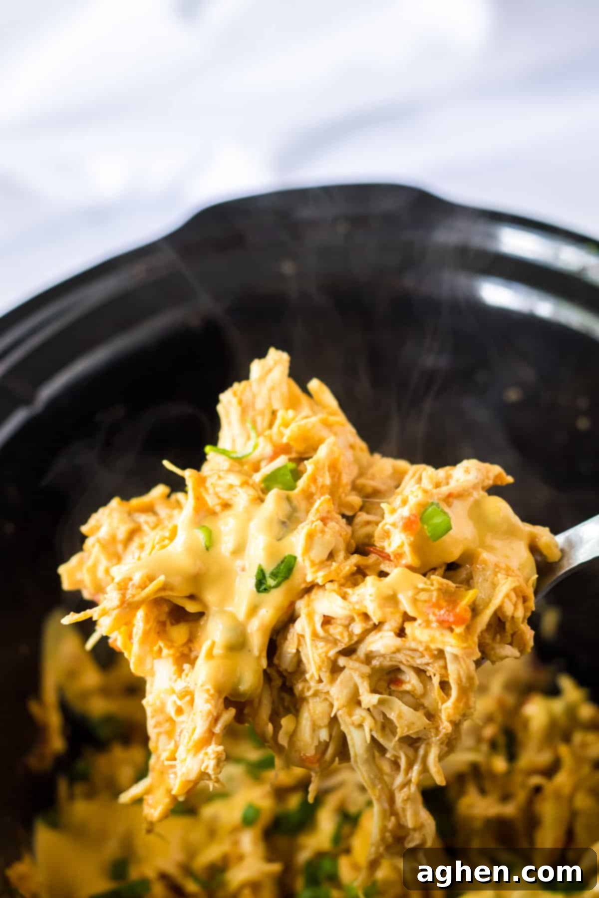 A spoon scooping creamy, cheesy queso chicken out of the slow cooker, ready to be served.