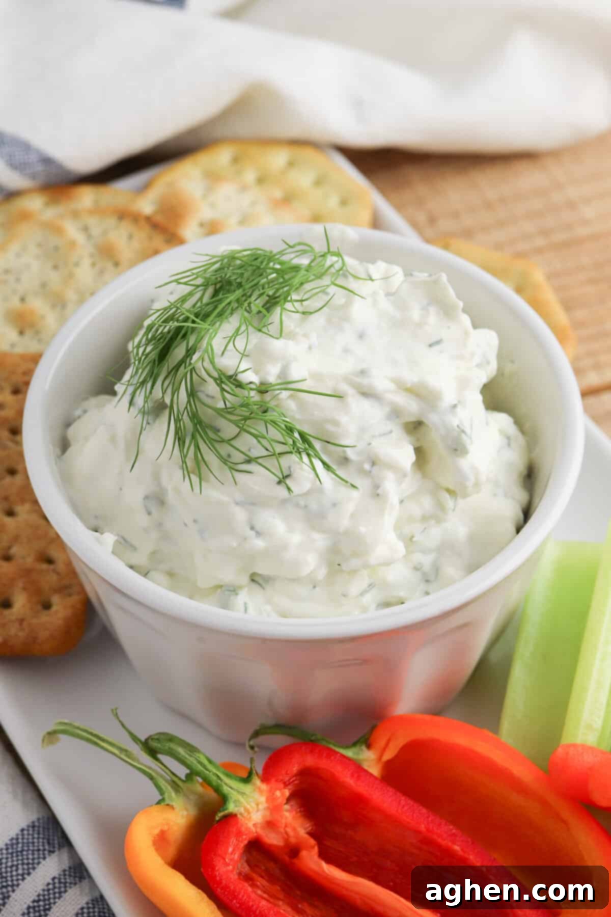 Cream cheese dill dip garnished with fresh dill sprig and served with crackers and fresh peppers and celery for dipping.