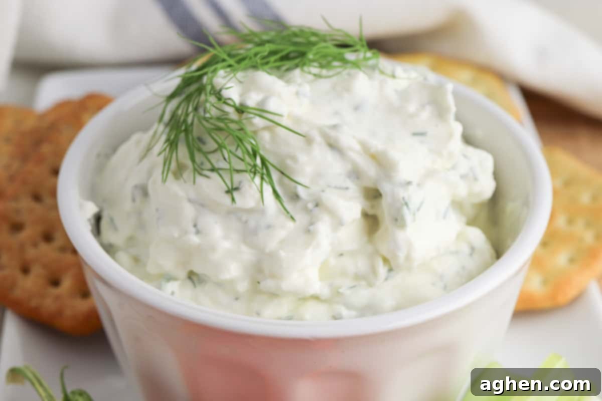 Creamy dill dip garnished with a sprig of fresh dill and served in a bowl with crackers for dipping.