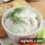 Cream cheese dill dip garnished with fresh dill sprig and served with veggie sticks and crackers for dipping.