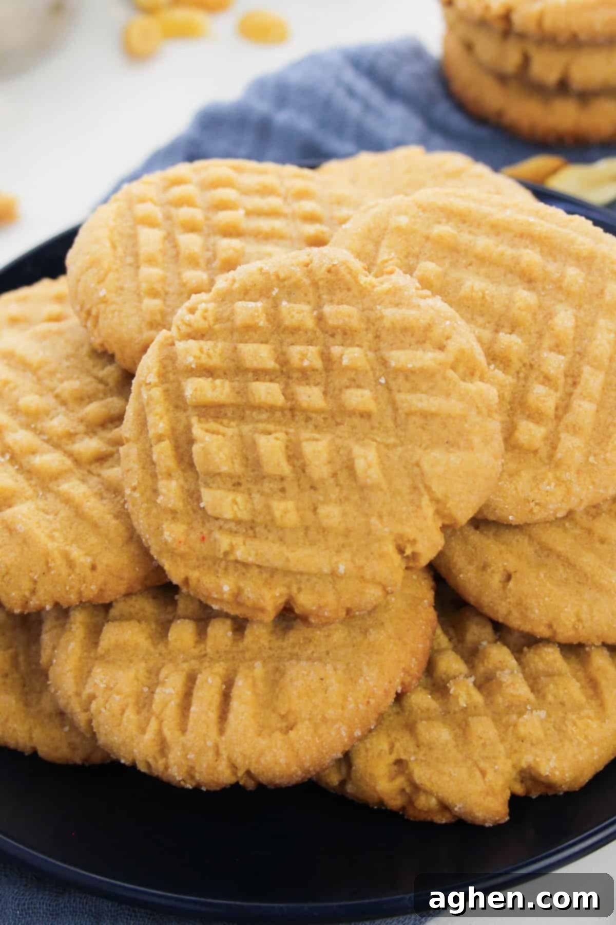 Batch of cake mix peanut butter cookies with criss-cross pattern pressed in the top piled on a black plate.