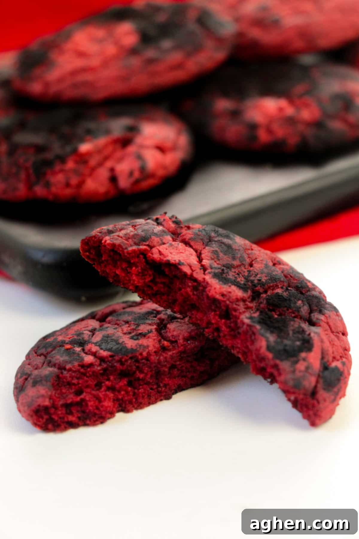Devil's Delights 3 Close-up of red and black crinkle cookies on a wooden platter with one cookie broken in half to show its vibrant red velvet interior, highlighting the striking contrast.