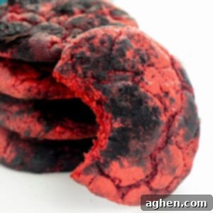 Devil's Delights 7 Red velvet cookies coated with black cocoa powder for a crinkle cookie effect. One cookie has a bite taken out of it to reveal the inside of the soft red velvet cake cookie.