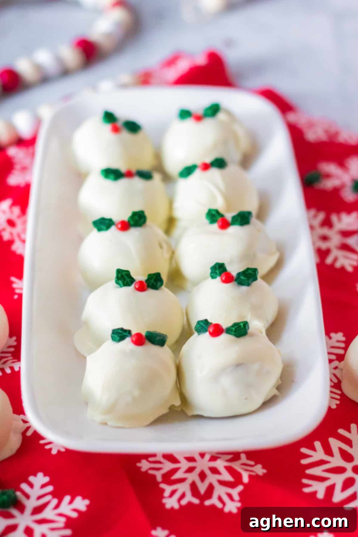 Snickerdoodle truffles coated in white chocolate, topped with a christmas sprinkle, and served on a white tray surrounded by holiday decor.
