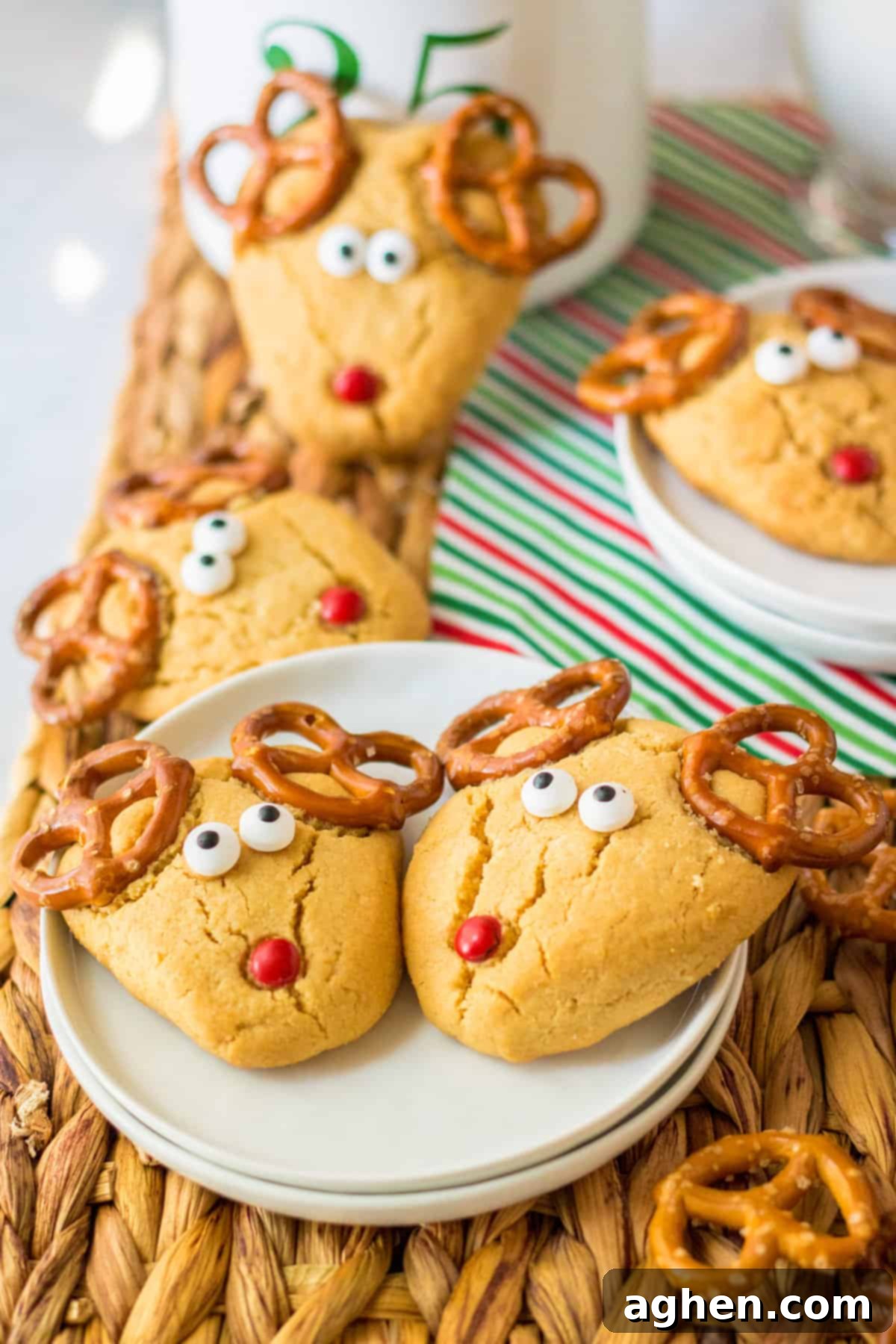 Peanut butter cookies shaped into an upside down triangle and decorated to look like Rudolph with pretzel antlers, candy eyes, and a red nose.