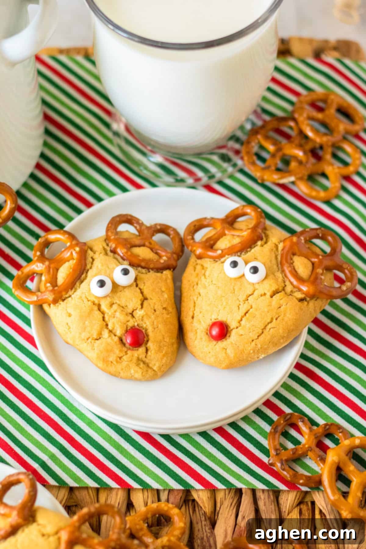 Two peanut butter reindeer cookies on a white plate with a large glass of milk.