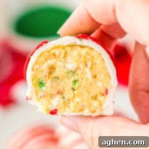 A hand holds a Little Debbie Christmas Tree Cake Ball, cut in half to showcase its vanilla cake center dotted with red and green sprinkles, ready for a festive bite.