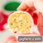 A hand holds a Little Debbie Christmas Tree Cake Ball, cut in half to beautifully reveal its vanilla cake center dotted with red and green sprinkles.