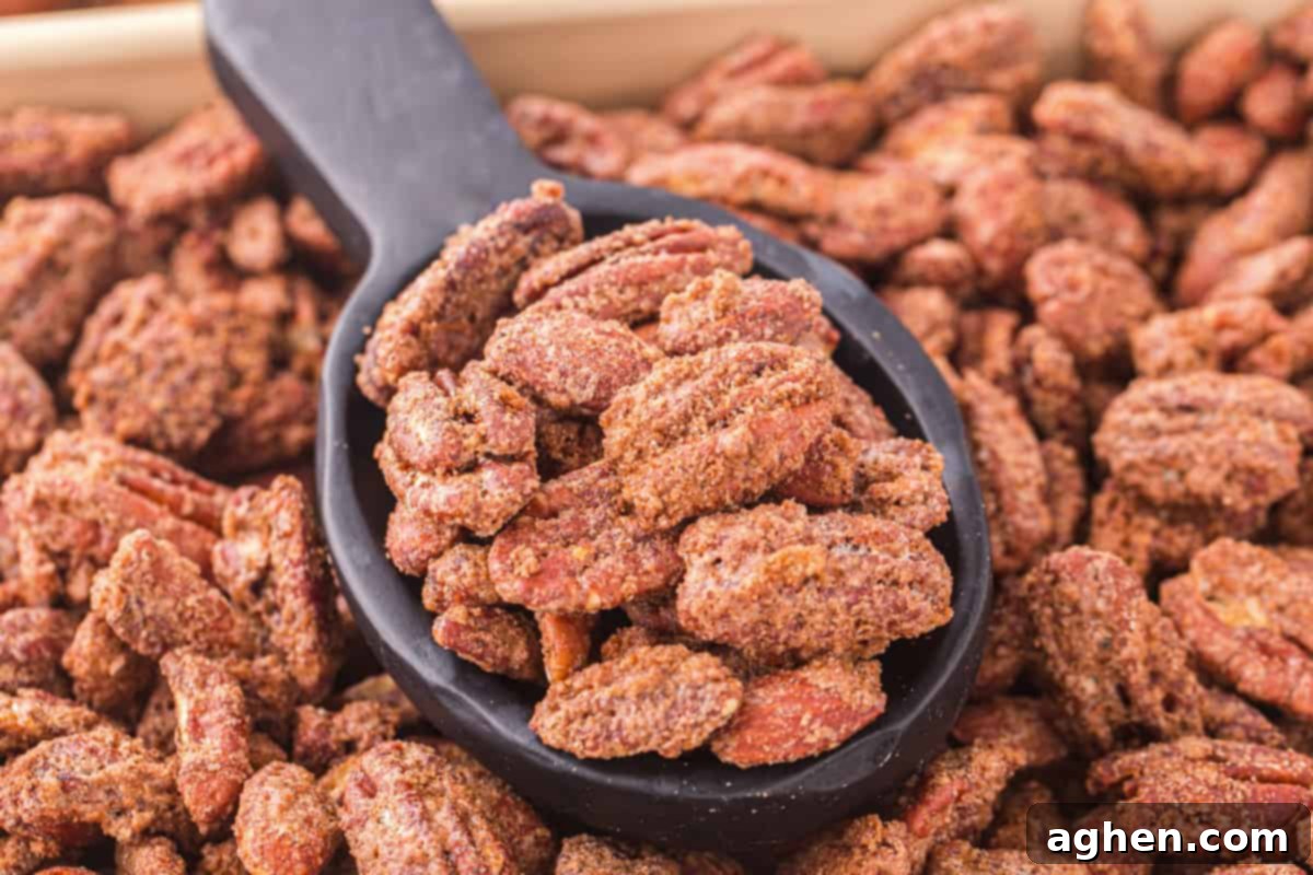 Cinnamon almonds and pecans on a sheet pan with some scooped into a black spoon, showcasing their delicious coating.