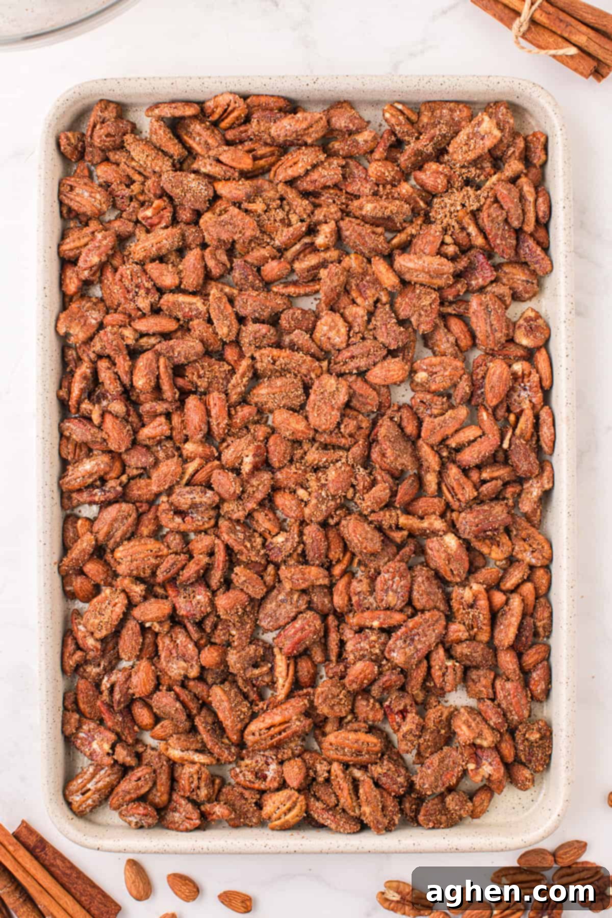 Coated nuts spread evenly in a single layer on a baking sheet, ready for the oven.