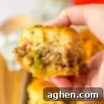 Bite-Sized Philly Cheesesteak Bliss 12 Hand holding a ground beef philly cheesesteak slider on a Hawaiian Roll with peppers and onions.