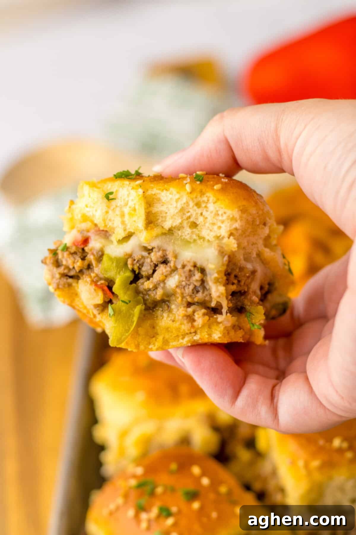 Bite-Sized Philly Cheesesteak Bliss 3 Hand holding a ground beef philly cheesesteak slider with peppers and onions. Serving suggestion with fries.
