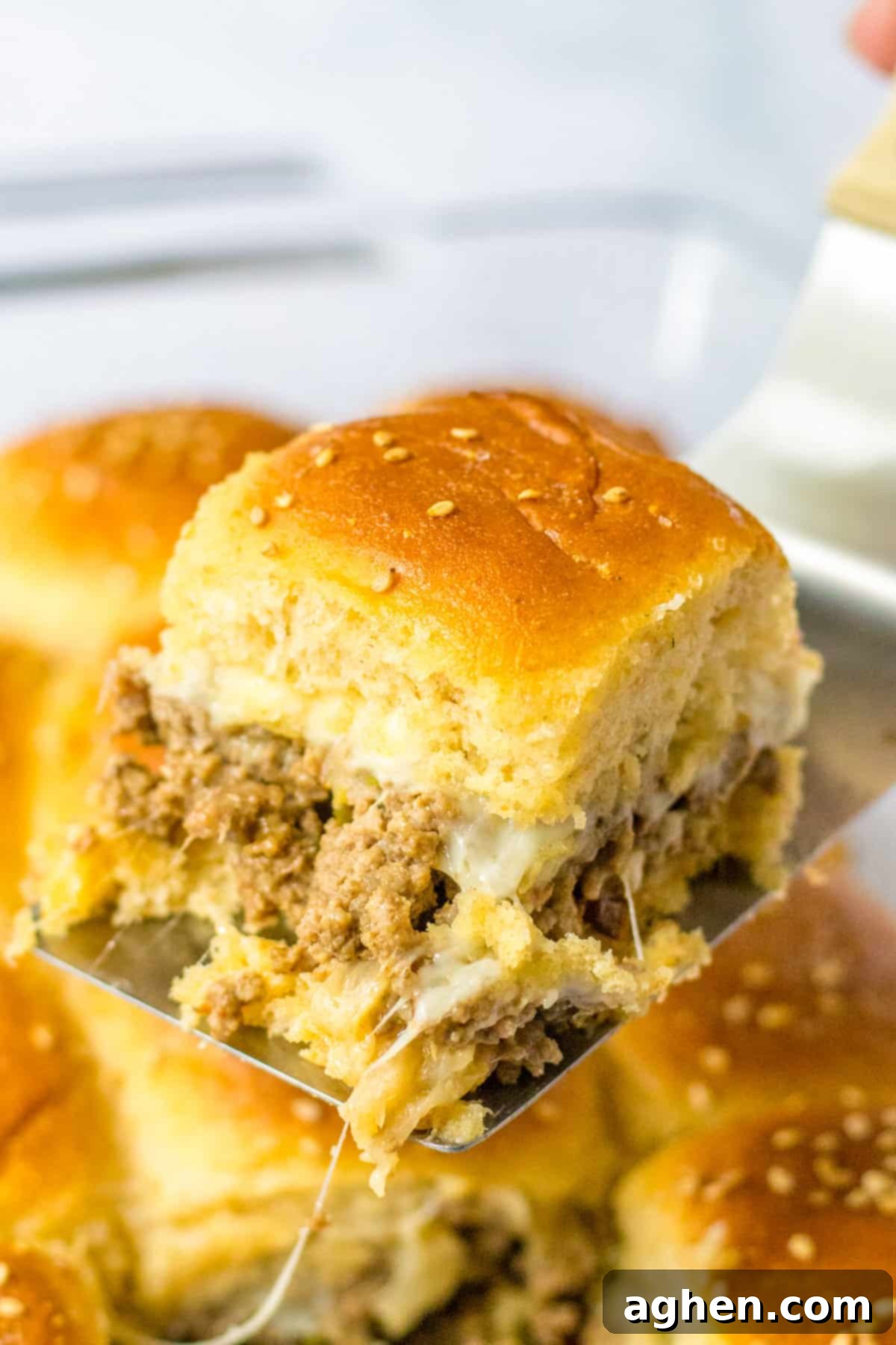 Bite-Sized Philly Cheesesteak Bliss 9 Hamburger Philly cheesesteak slider being lifted from dish with metal turner, showing melted cheese and filling.