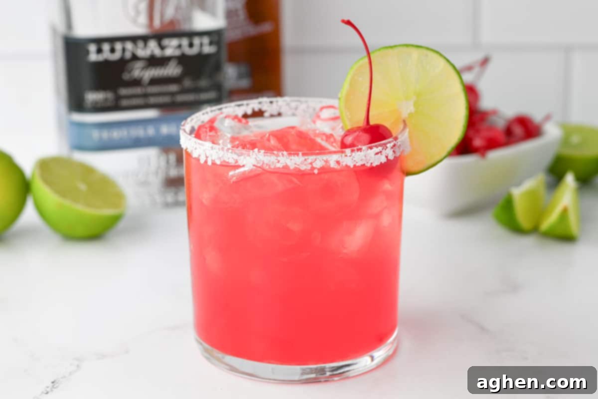 Blush Margarita 6 Pink Margarita cocktail in a rocks glass with a salted rim and lime wheel and cherry for garnish. Lime wedges and a bottle of tequila are in the background.