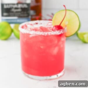 Blush Margarita 7 Pink Margarita drink in a rocks glass with salted rim and lime wheel and maraschino cherry garnish.