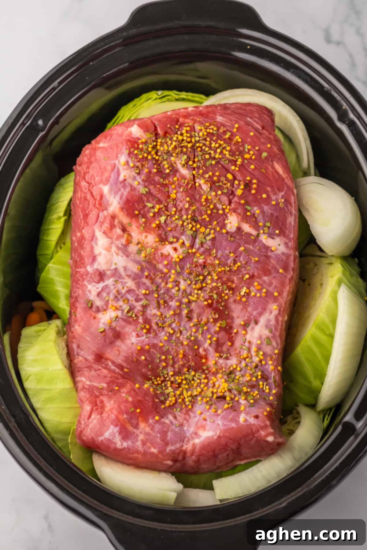 Corned beef in crockpot surrounded by cabbage, onions, and carrots.