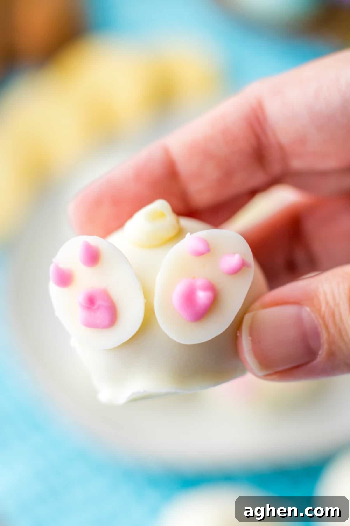 A hand gently holds an adorable Bunny Oreo Ball candy, showcasing its white chocolate coating and charming bunny butt decoration.