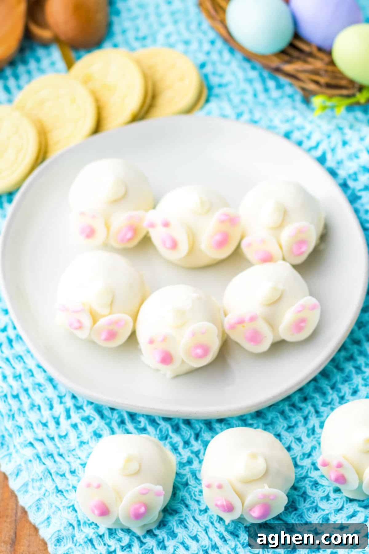 An overhead view of charming bunny truffles, each coated in smooth white chocolate and adorned with delicate candy feet and swirling tails. They are surrounded by cheerful lemon cookies and festive Easter decorations, creating a delightful holiday spread.