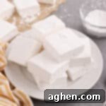 Fluffy homemade marshmallows piled on white plate coated in powdered sugar.