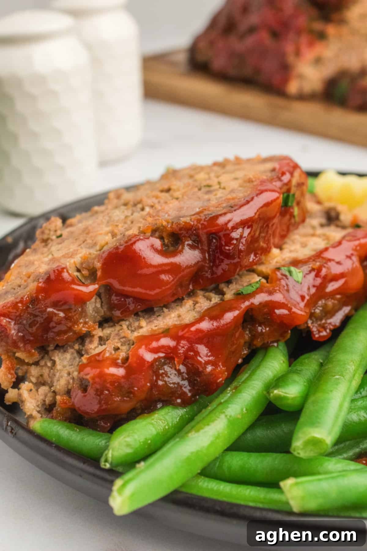 Two slices of glazed lipton onion soup metloaf with green beans on a black plate.