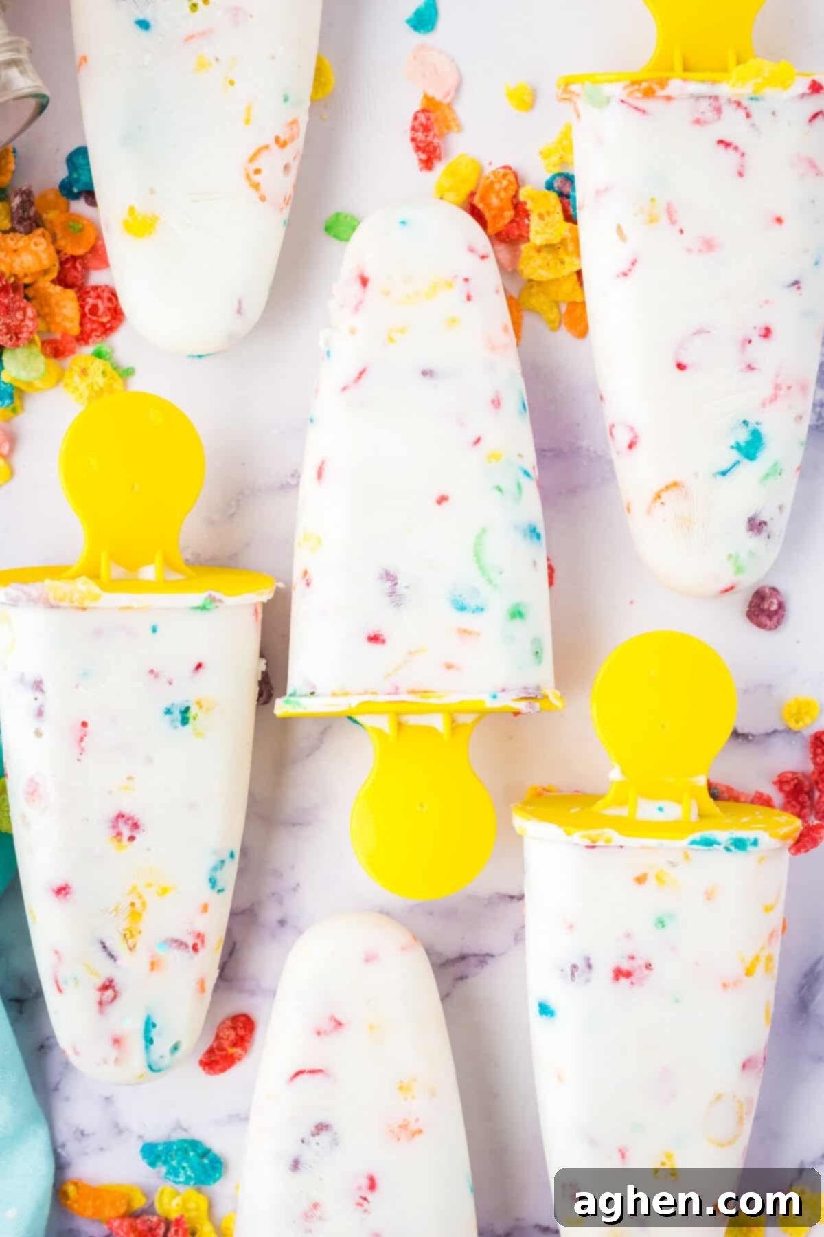 Homemade fruity Pebbles cereal Greek yogurt popsicles with yellow handles. The colorful cereal can be seen throughout the white ice pops.