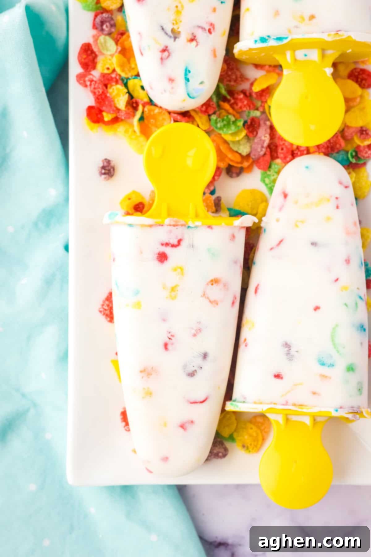 Frozen Greek yogurt pops with colorful Fruity Pebble cereal on a white tray, showcasing the vibrant colors.