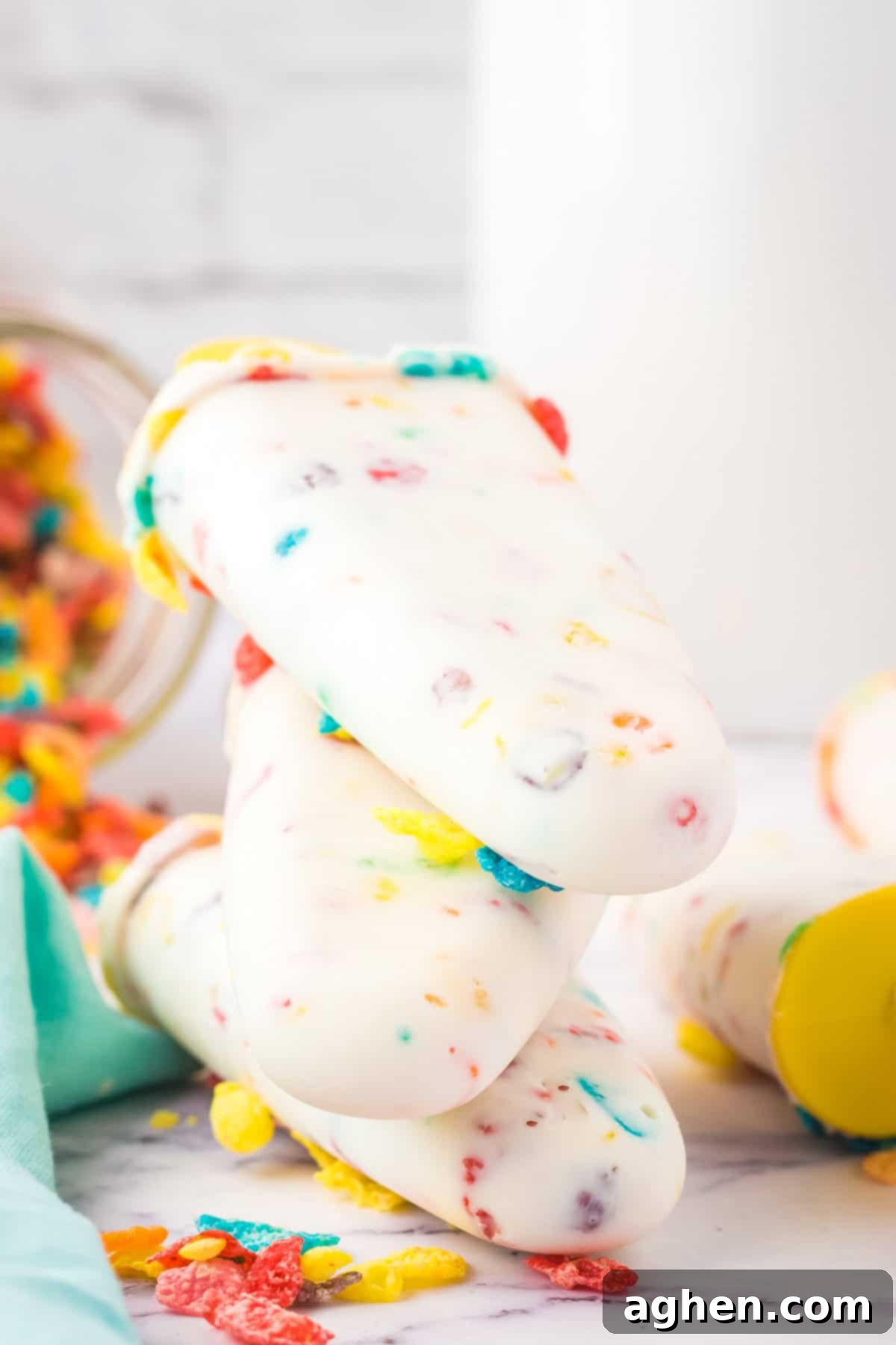 Rainbow cereal and yogurt breakfast popsicles stacked on top of one another in front of a large glass of milk, emphasizing breakfast appeal.