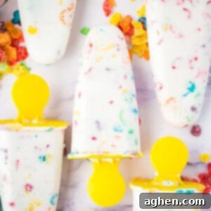 Homemade fruity Pebbles cereal Greek yogurt popsicles with yellow handles. The colorful cereal can be seen throughout the white ice pops.