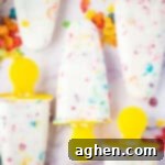Homemade fruity Pebbles cereal Greek yogurt popsicles with yellow handles. The colorful cereal can be seen throughout the white ice pops.