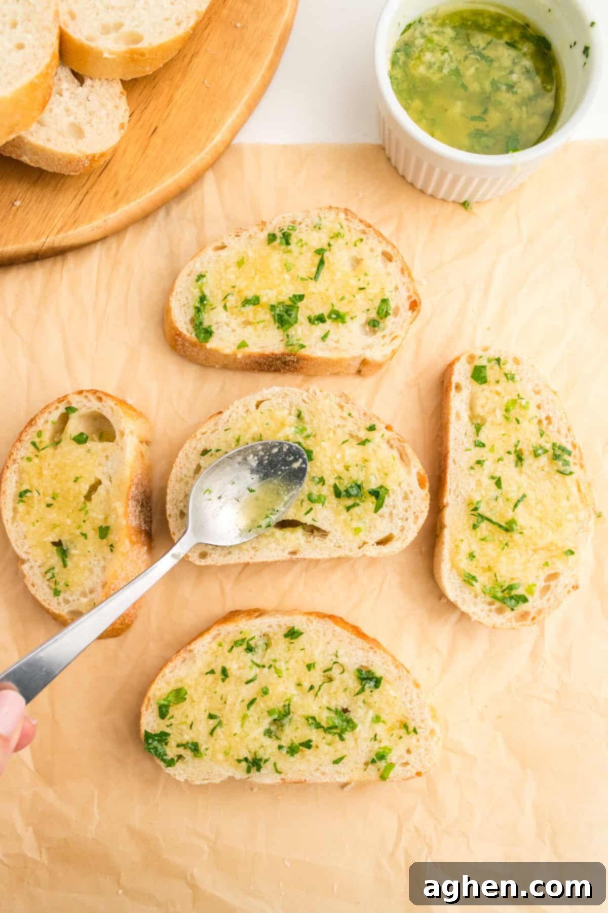 Slices of garlic bread on parchment paper with butter mixture being spooned on to them.
