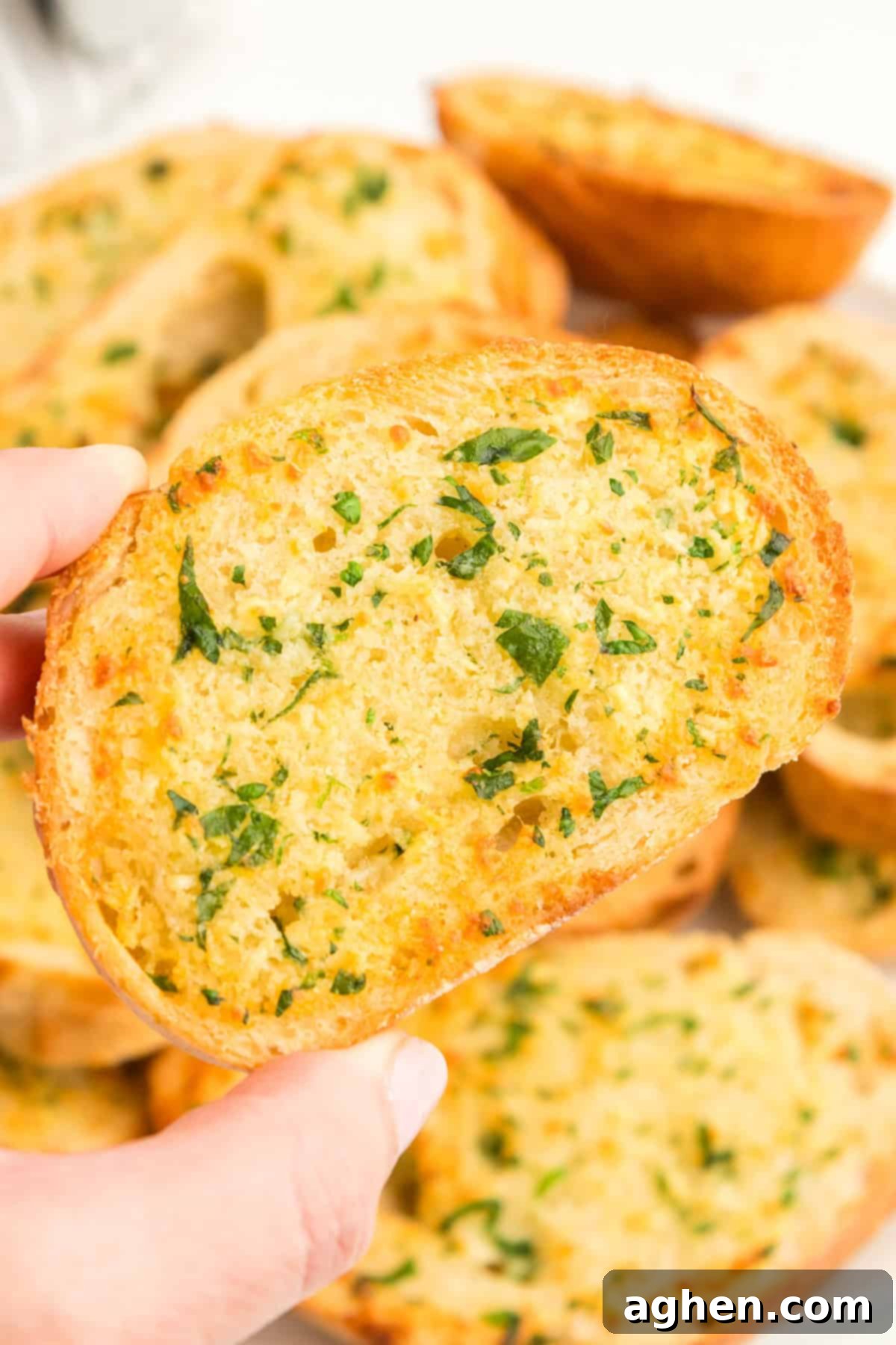 Hand holding piece of thick and crispy garlic bread with parsley garnish.