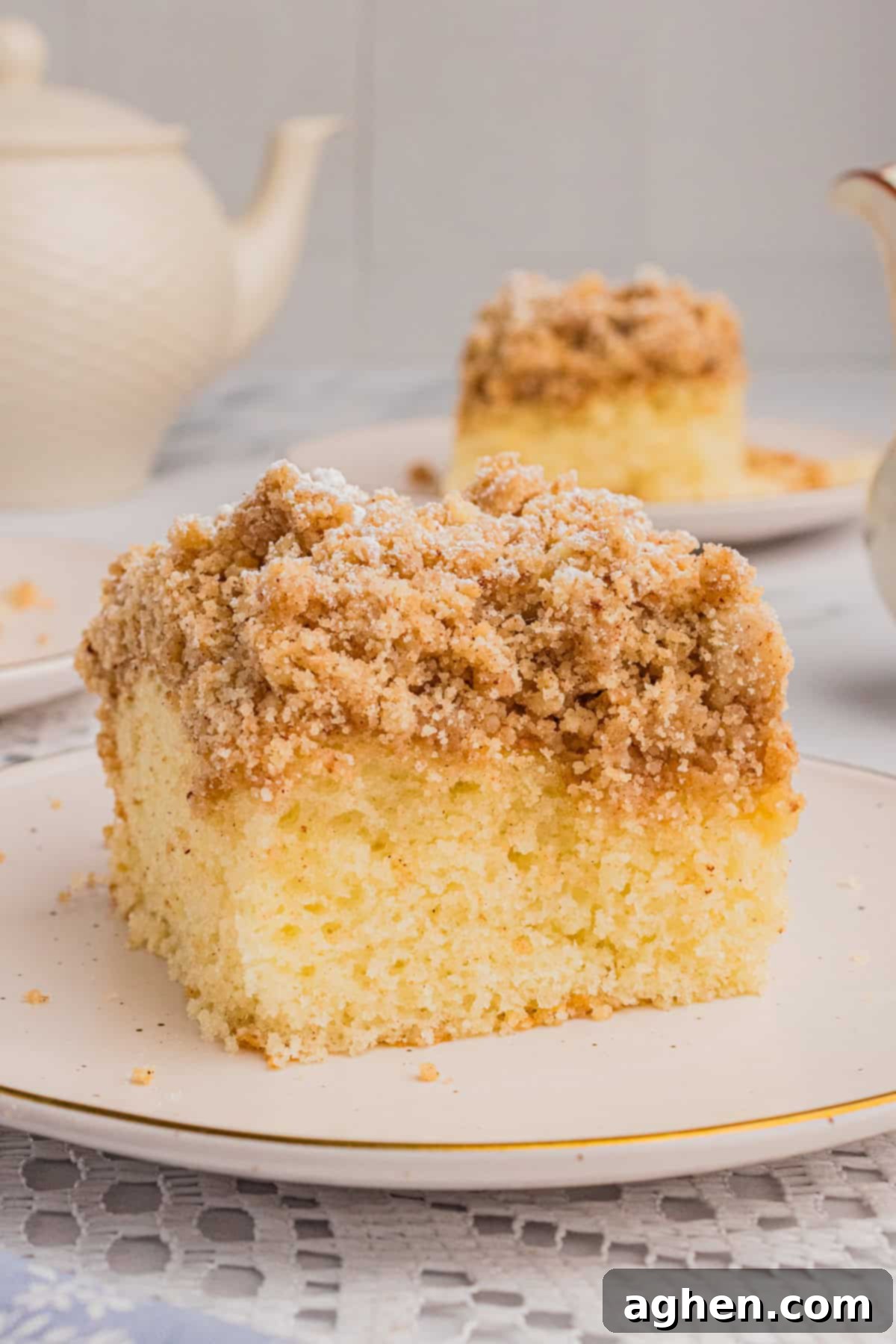 Simple Crumb Cake Perfection 2 Slice of New York style crumb cake with thick layer of crumb topping. Another slice and a teapot are in the background.