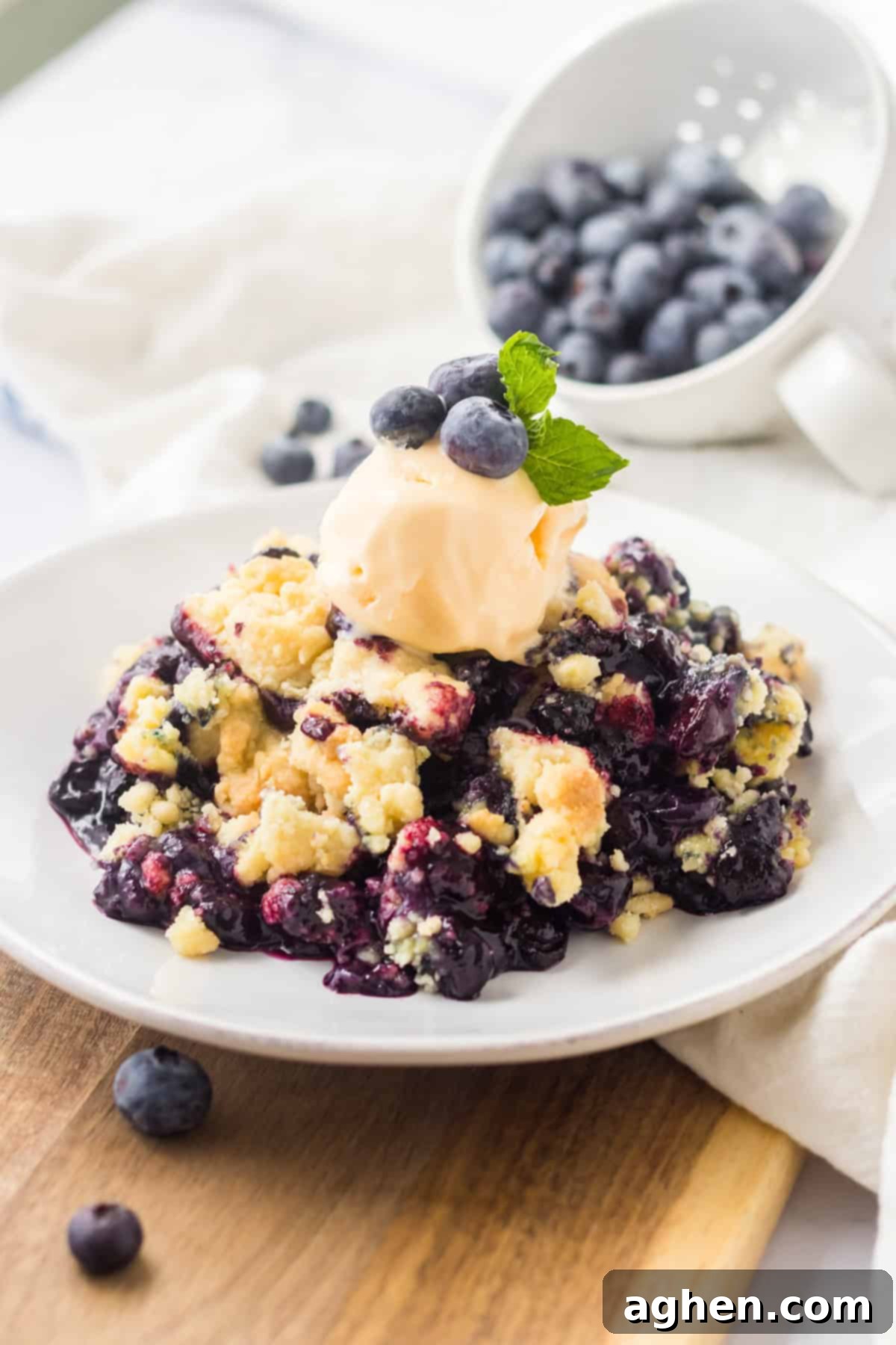 4 Ingredient blueberry cobbler served on a white plate and topped with a scoop of vanilla ice cream and fresh blueberries.